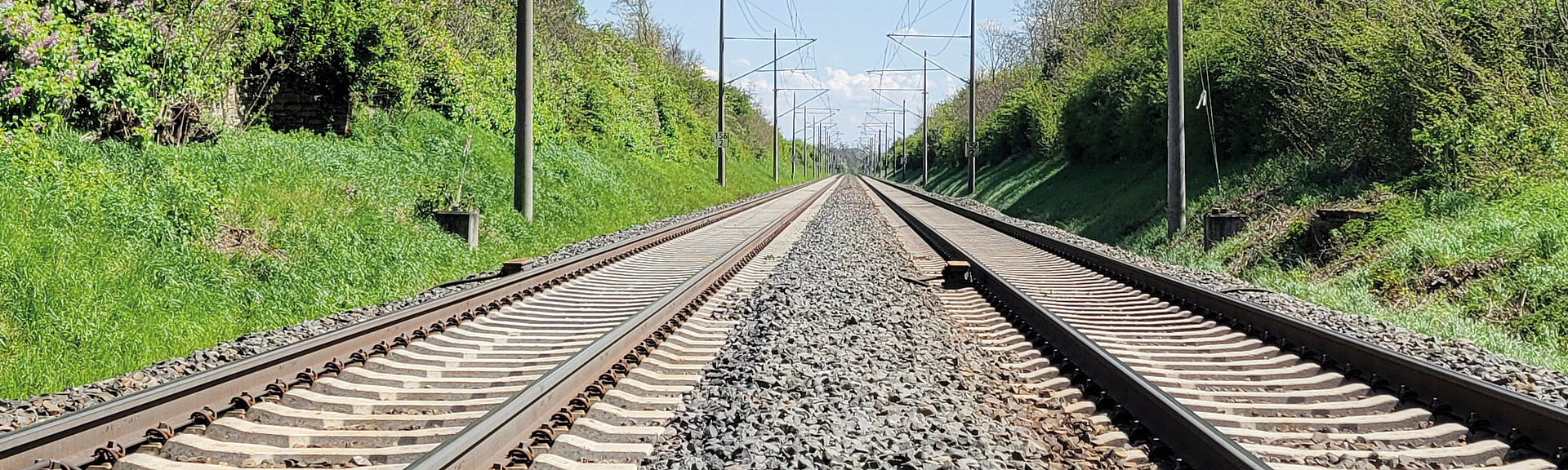 Zwei nebeneinander liegende Gleise an einer Eisenbahnstrecke mit Oberleitungen.