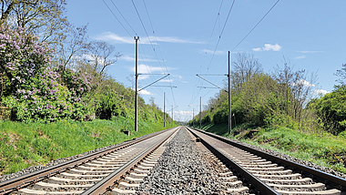 Zwei nebeneinander liegende Gleise an einer Eisenbahnstrecke mit Oberleitungen.