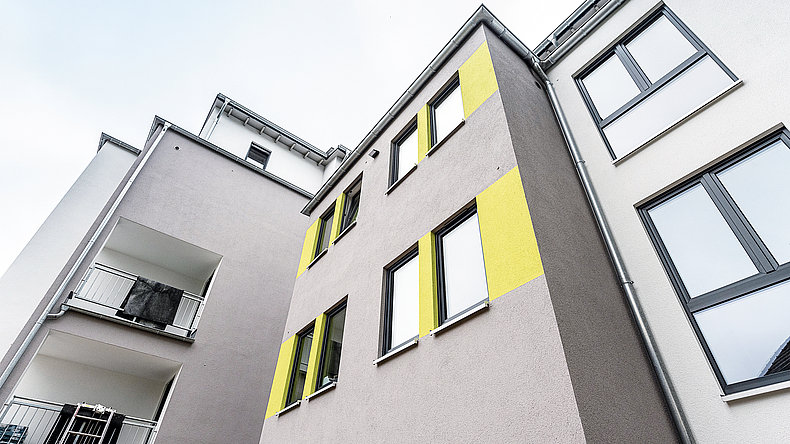 Die Außenwände haben eine brandschutztechnisch wirksame Bekleidung aus nicht brennbaren Baustoffen in K₂30 gemäß DIN EN 13501-2 in Anlehnung an die Musterholzrichtlinie. Blick von unten auf verschachteltes, mehrstöckiges Gebäude
