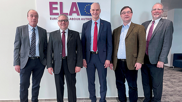 Bernd Merz, Mathias Neuser, Michael Kirsch, Walter Sailer und Prof. Karl-Heinz Noetel vor dem ELA-Plakat Gruppenfoto mit fünf Männern vor dem ELA-Plakat