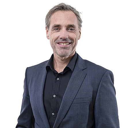 Lächelnder älterer Mann mit kurzen Haaren und Dreitagebart in schwarzem Hemd und dunkelblauem Jacket
