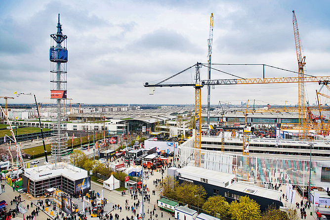 Bei jeder bauma ein Anziehungspunkt: das großzügige Freigelände mit großen Baumaschinen Blick von weitem auf das Messegelände mit Messehallen und Kränen.