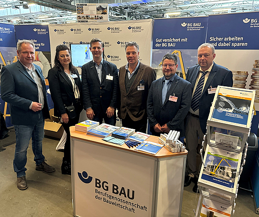 Team der BG BAU am Infostand auf der Fachtagung Abbruch 2024 Gruppe von sechs Personen an einem Infostand mit Logo der BG BAU