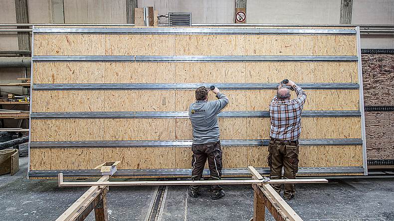 Zwei Männer arbeiten an einer Wohnungstrennwand in einer Fertigungshalle.