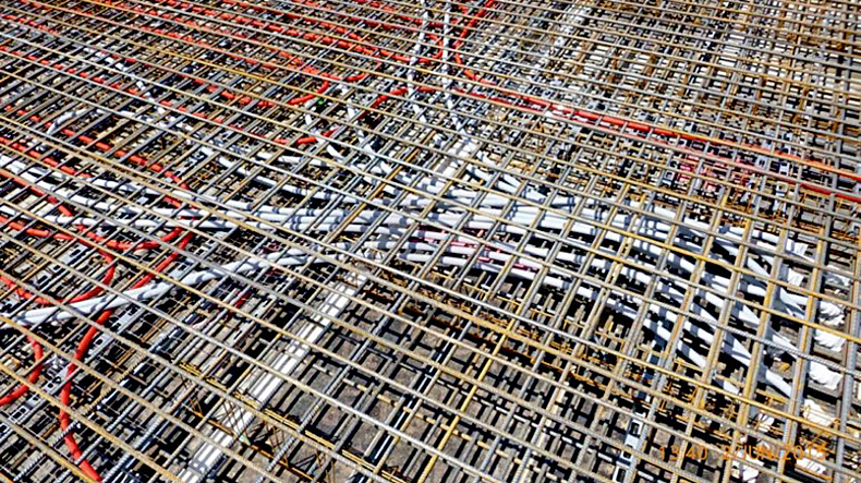 Bewehrungsraster, unter dem sich silberne Rohre befinden.