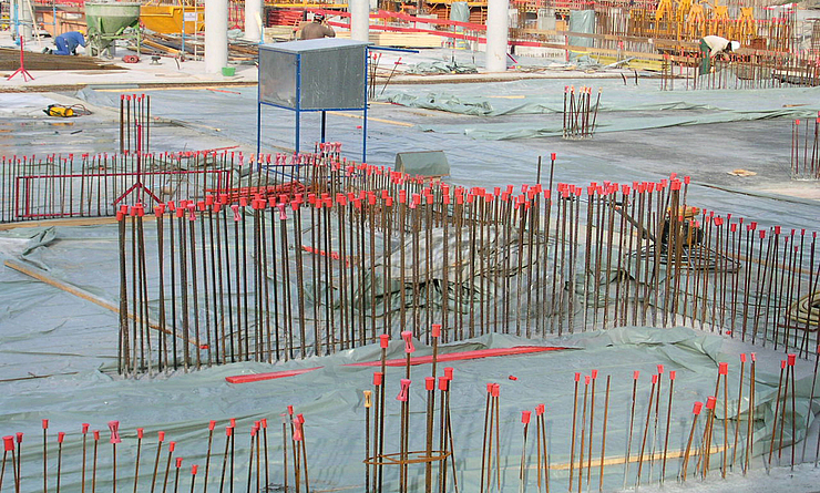 Bewehrungsstäbe mit roten Schutzkappen auf einer Baustelle zur Sicherung freiliegender Stangenenden.