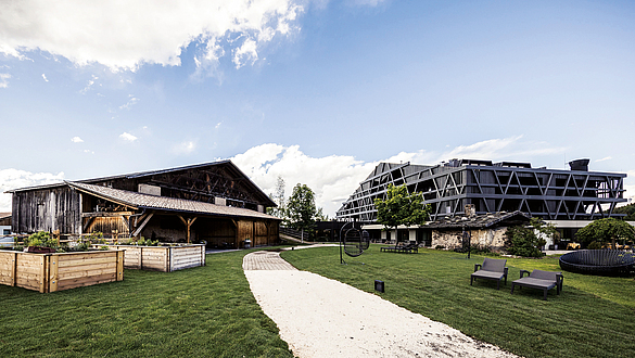 Weitläufiges, grünes Gelände mit einem alten Holzgebäude und einem Gebäude mit moderner Fassadenkonstruktion aus Holz daneben.