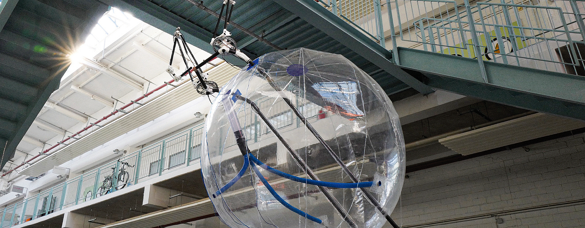 Ballon-Kopter, der in einer Halle unter einem Verbindungssteg schwebt.
