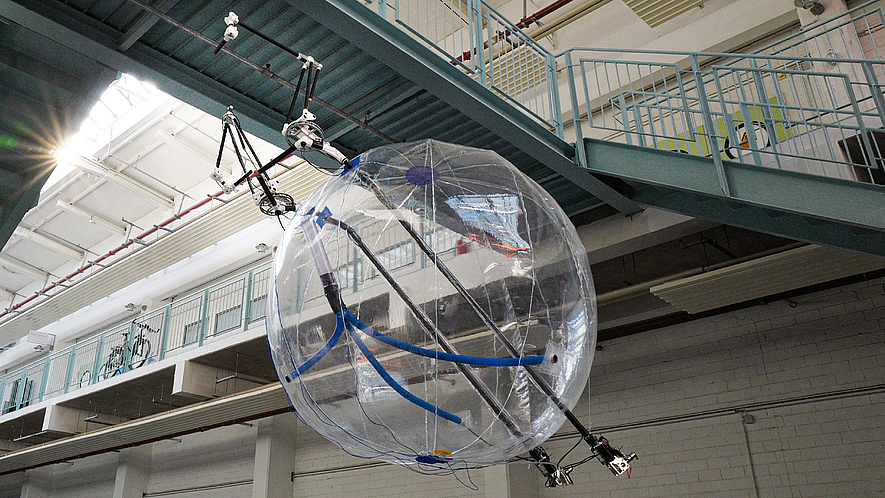 Ballon-Kopter, der in einer Halle unter einem Verbindungssteg schwebt.