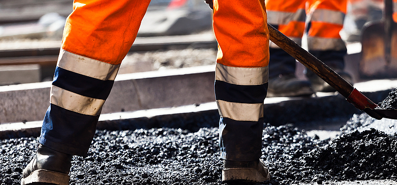 Heißverarbeitung von Bitumen Bauarbeiter mit Schaufel beim Straßenbau und der Verarbeitung von Bitumen auf der Straße.