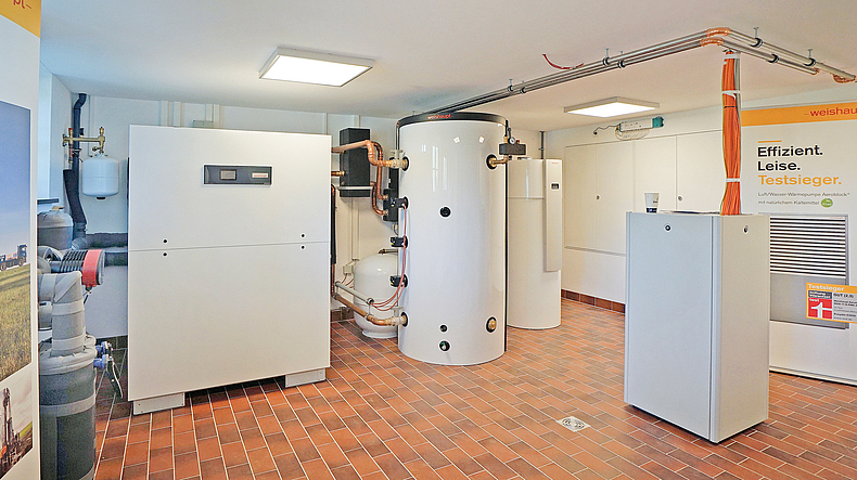 Heizungs- und Wärmetechniksystem in einem Technikraum mit mehreren weißen Anlagen und Rohrleitungen.