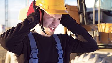 Mann steht auf einer Baustelle und drückt seinen Kapselgehörschutz gegen die Ohren.