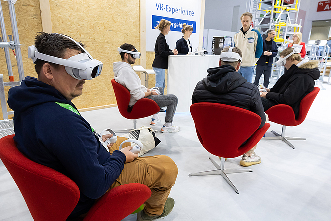Mehrere Messebesucher testen im Sitzen mit VR-Brillen die Anwendung Virtual Reality aus.